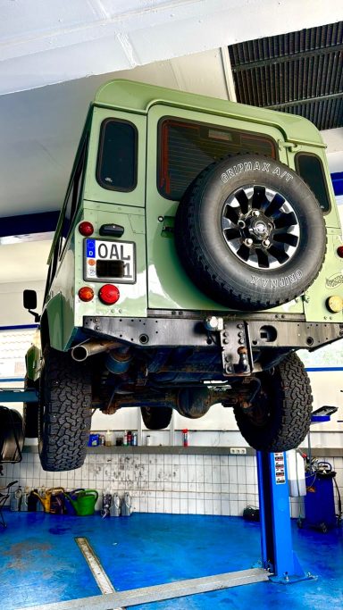 Grüner Geländewagen, auf einer Hebebühne mit sichtbarem Ersatzrad.
